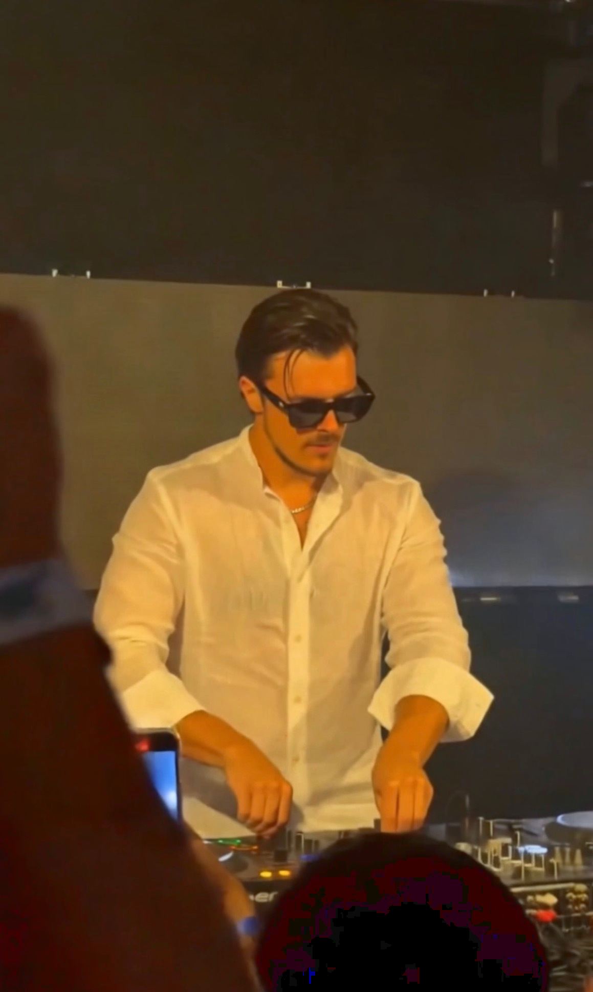 ROOM:SRVC DJ Sascha behind the decks in a white shirt, seen from the crowd